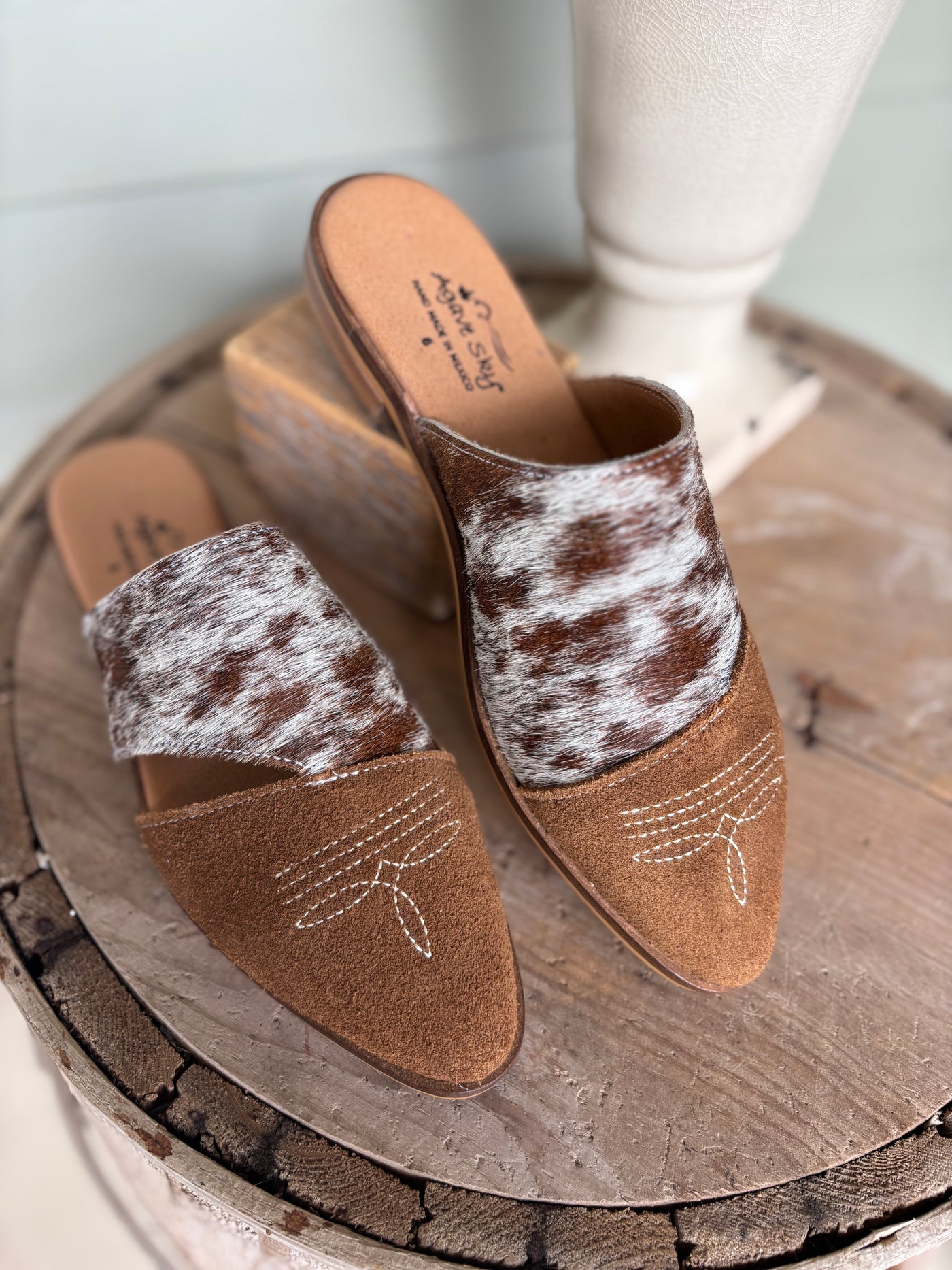 Pair of brown mules with cowhide pattern on a wooden surface
