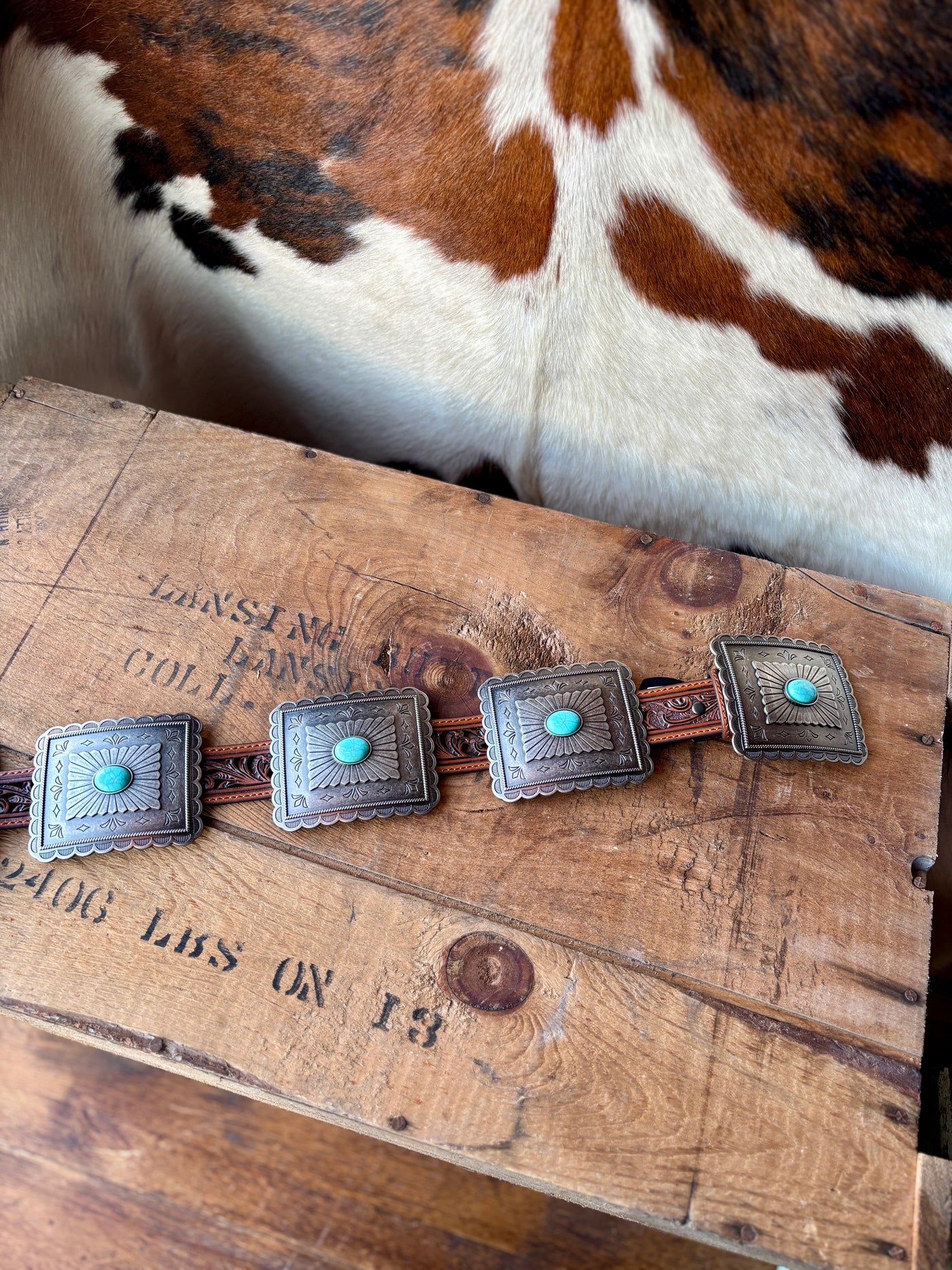 The Ariat Tara Turquoise Rectangle Concho Belt laid out on a wood surface showing the intricate carved conchos and leather belt strap.