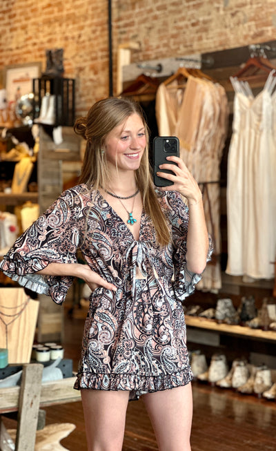 Our store employee, Grace, modeling the Aurora Paisley Tie Front, Bell Sleeve, Ruffled Romper paired with turquoise accessories for a chic, carefree summer outfit.