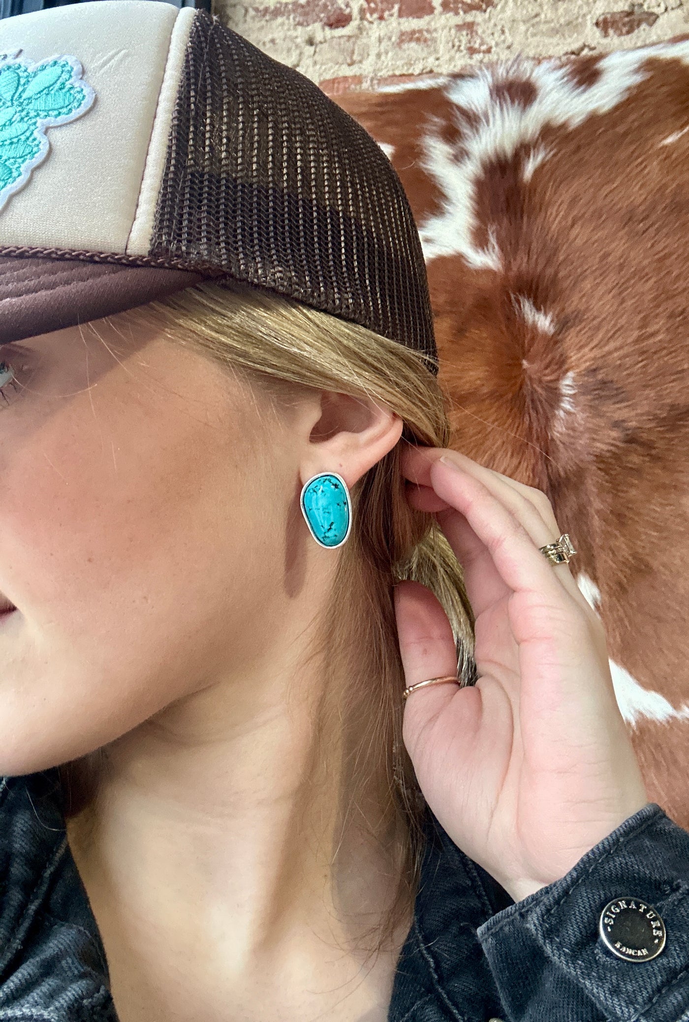 Oval-shaped faux turquoise stud earrings with silver-plated setting, Western-inspired jewelry modeled by woman to show size relevance.