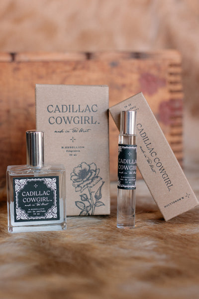 Photo of our glass bottle of Cadillac Cowgirl Perfume Spray with kraft box in background and the same scent in the roll-on glass container.