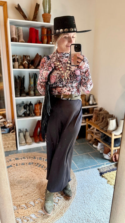 Woman modeling our Call You Later Maxi Skirt [Black] paired with a floral mesh top, boots, and cowboy hat.