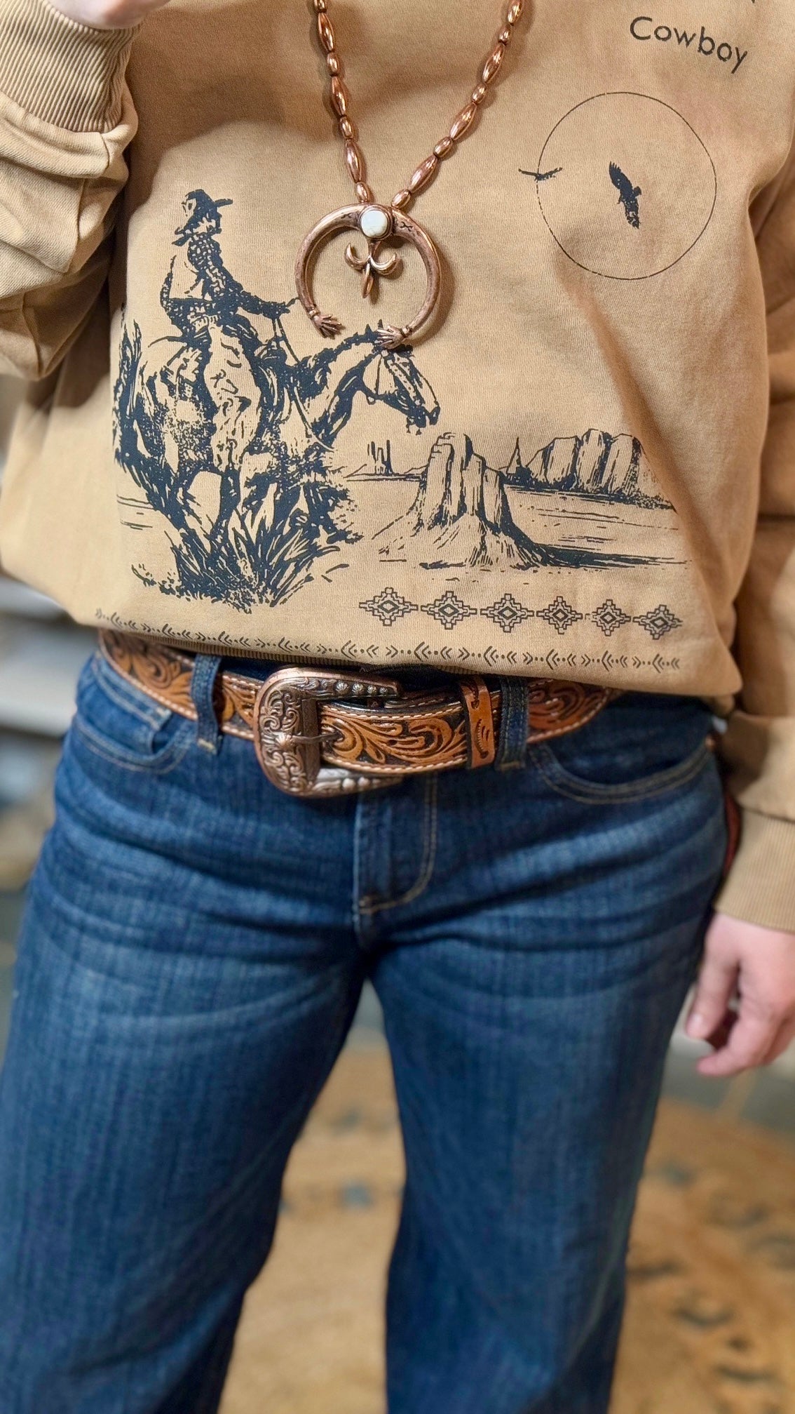 Close-Up of American Cowboy Desert Scene Graphic on Sweatshirt and Dahlia Tooled Leather Belt with intricate floral hand-tooling and brown whipstitch detailing.