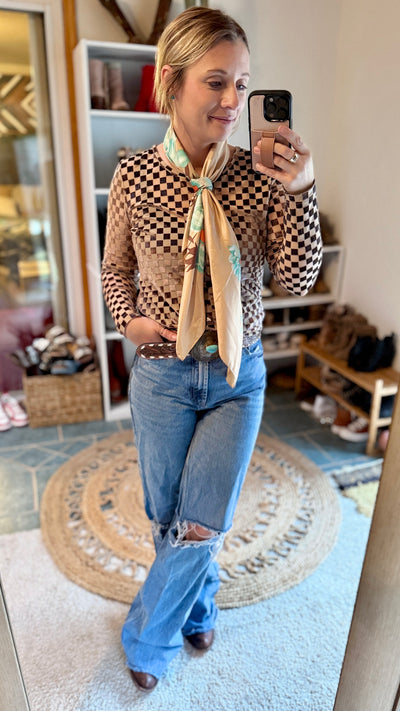 Model wearing the Championship Checkered Velvet & Mesh Top styled with cowboy boots, a leather belt, jeans and an oversized wild rag scarf.