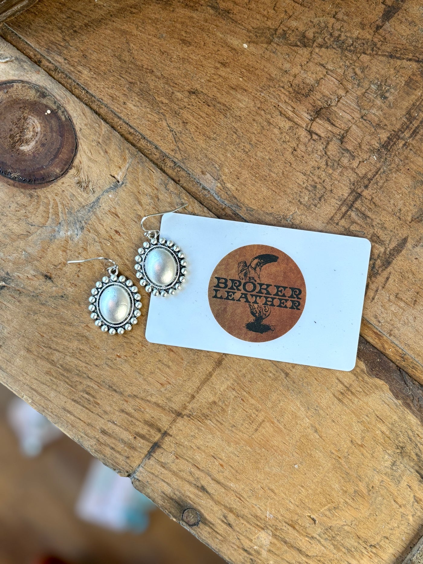 A flatlay of our Charlene Boho Oval Earrings next to our Broker Leather gift card for size reference.