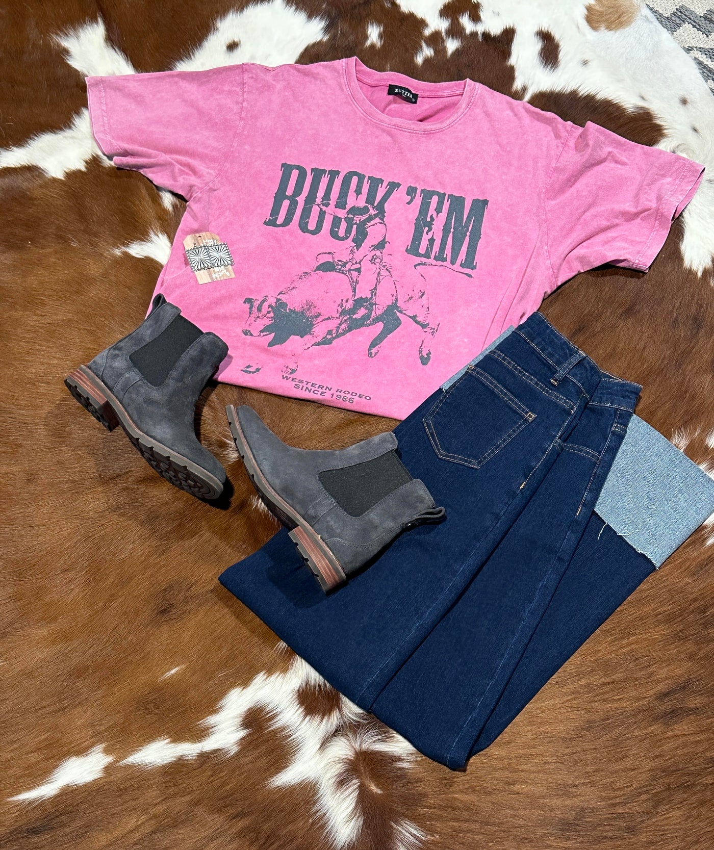 The Clide Buck 'em Graphic Tee on display paired with denim and the Ariat Wexford Boots, adding a playful and sassy touch to your casual wardrobe.