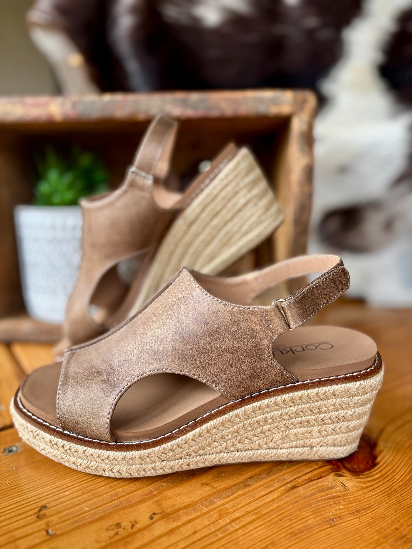 A pair of Corky's K Bye wedge sandals in tan color with a velcro slingback and a braided jute-wrapped wedge, displayed on a wooden surface.