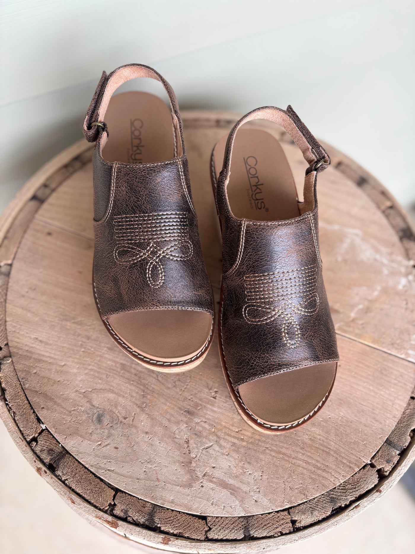 Pair of western brown sandals with boot stitch pattern on a wooden surface.