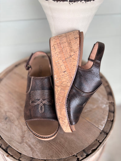 Pair of brown sandals with cork insole and boot stitch pattern on the camp displayed on a wooden surface.