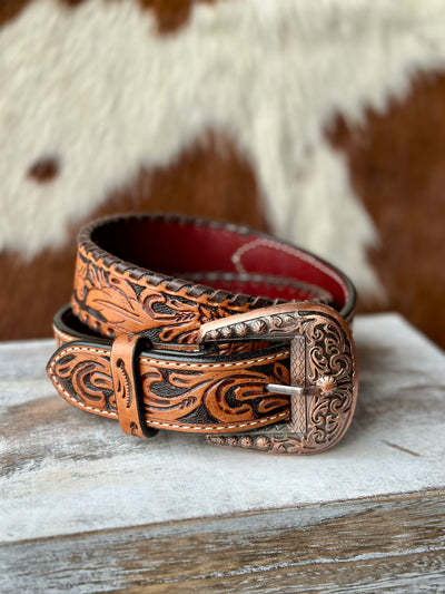 Western-style tooled leather belt with copper-colored engraved buckle, displayed on rustic background.