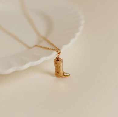 A gold Cowboy Boot Necklace on a gold chain available at Broker Leather in Waukon, Iowa.