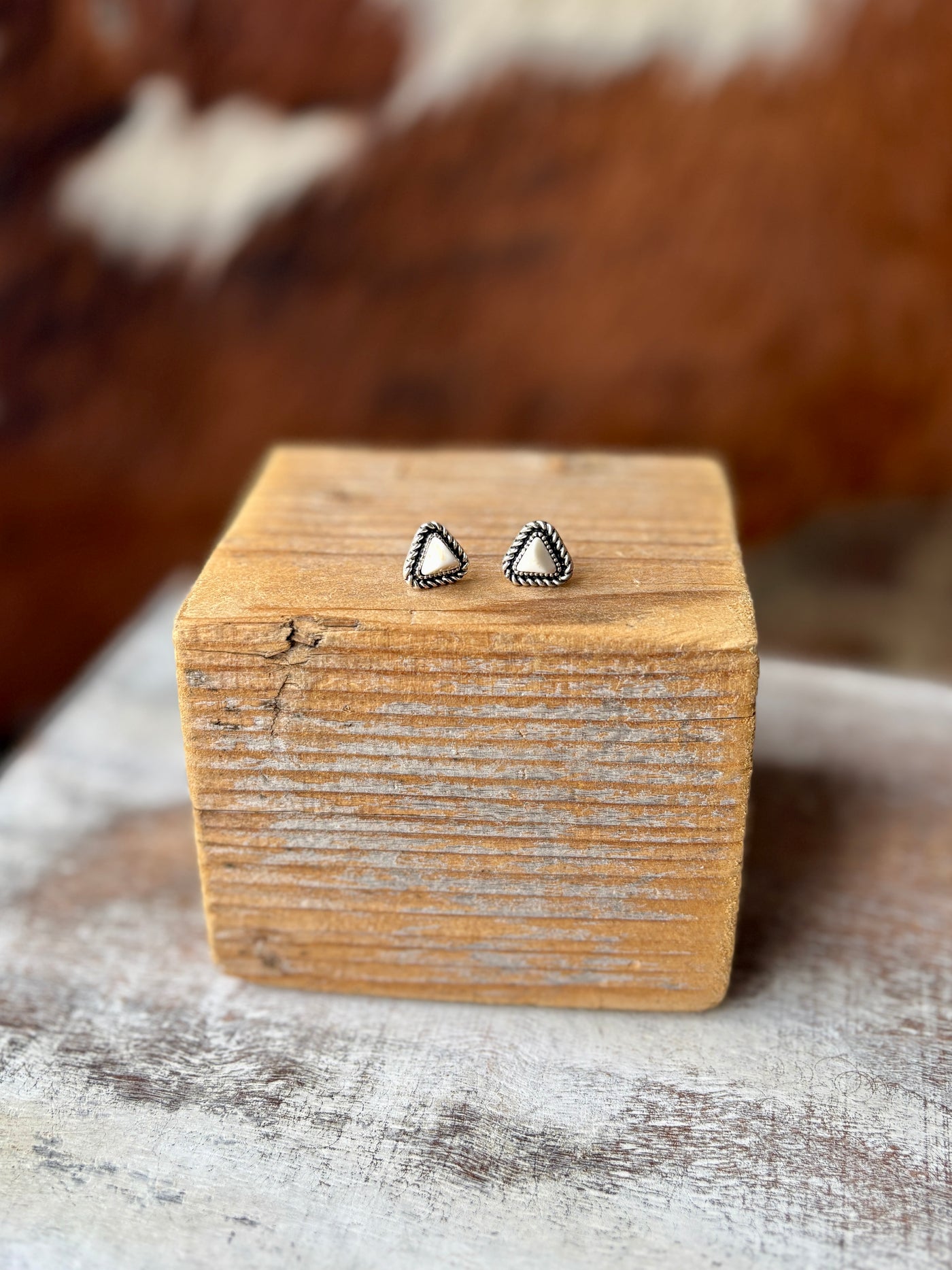 Western-inspired faux white buffalo stud earrings with intricate silver rope detail, displayed on wood.