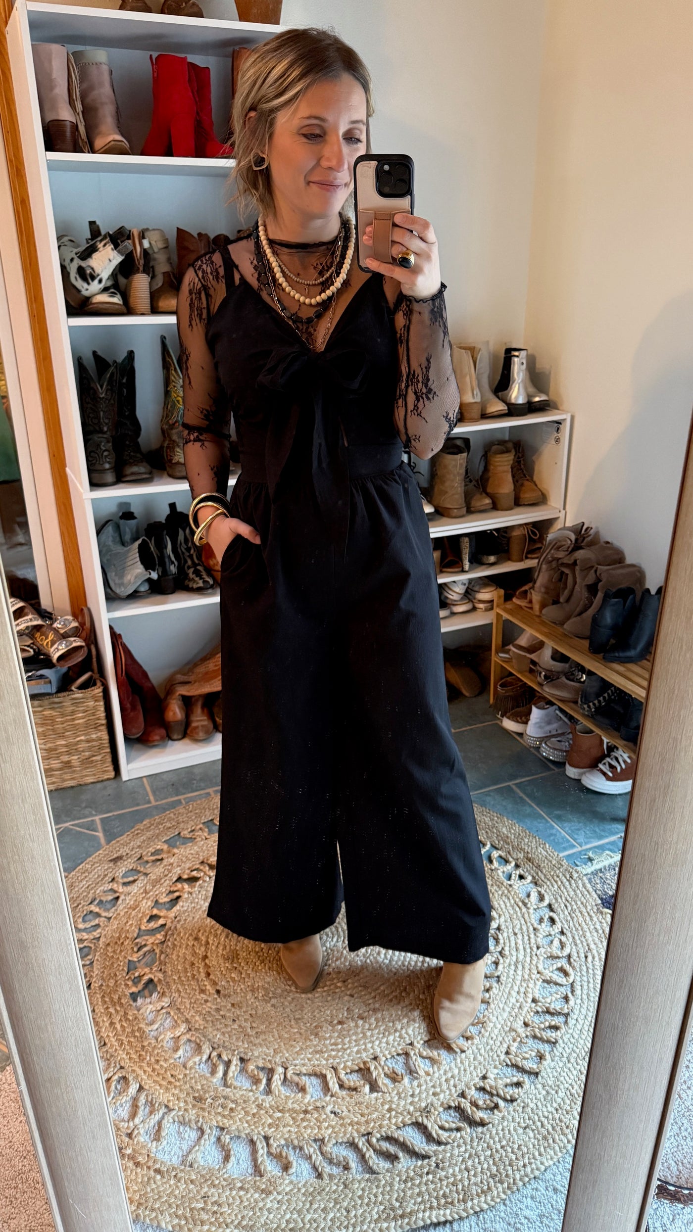 Broker Leather employee modeling the Dayton Bow Pant Jumpsuit with a lace undershirt and boots.