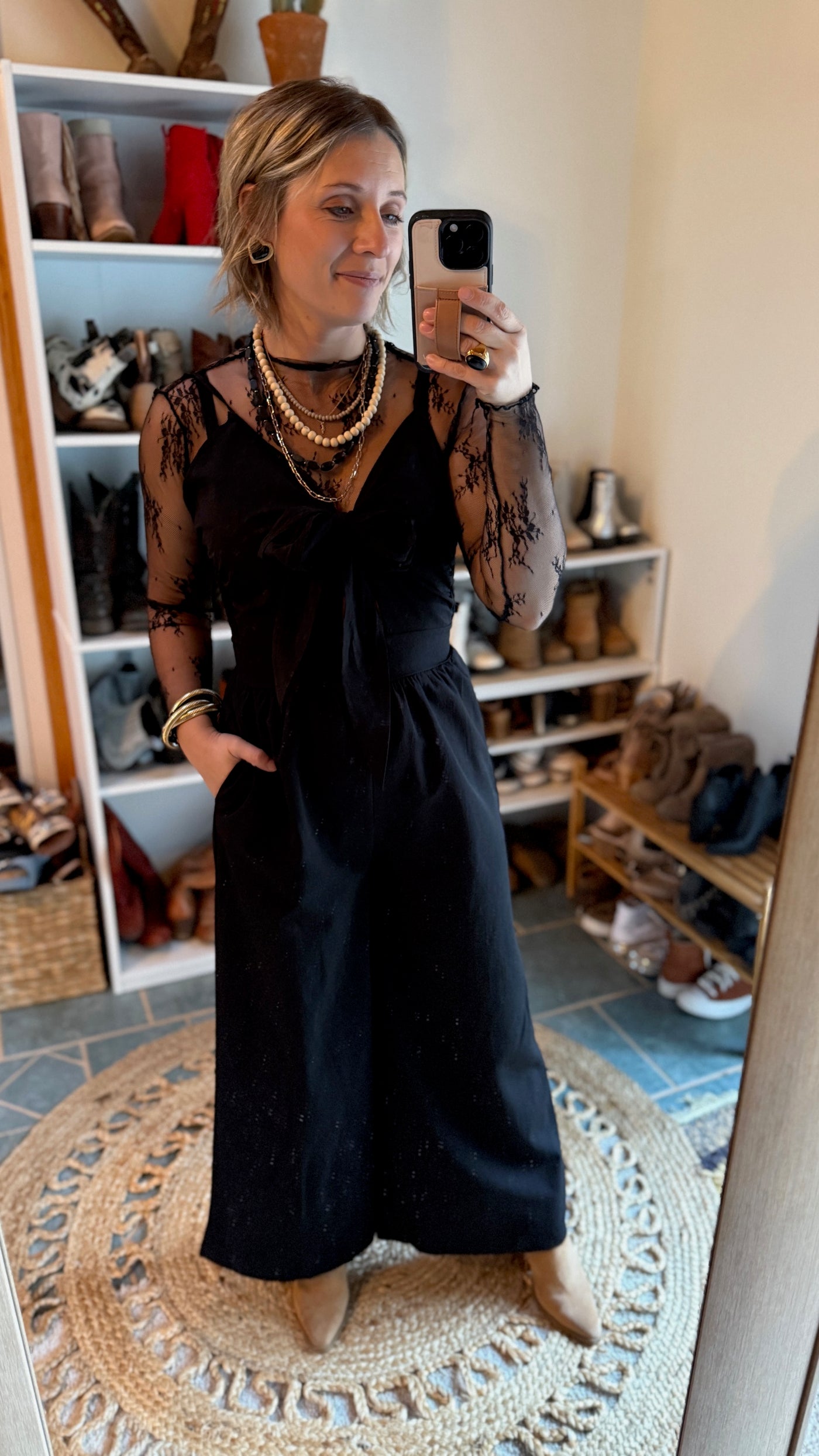 A Broker Leather employee modeling the Dayton Bow Pant Jumpsuit with statement necklaces and boots.