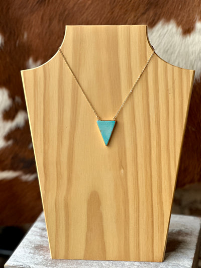 Faux turquoise and gold triangle necklace resting on weathered wood for a Western aesthetic.