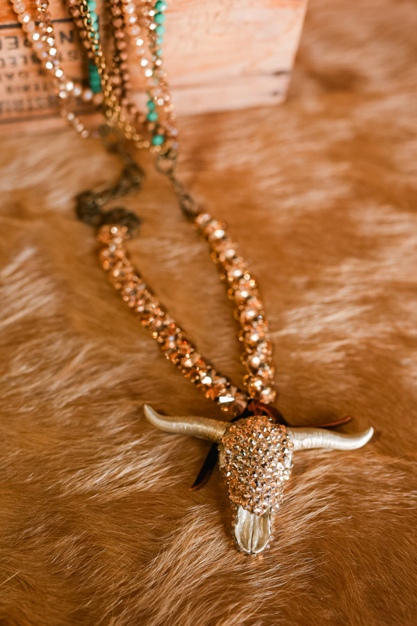 Flatlay photo of our beautiful Elliott Crystal Bull Skull Necklace on cowhide rug.