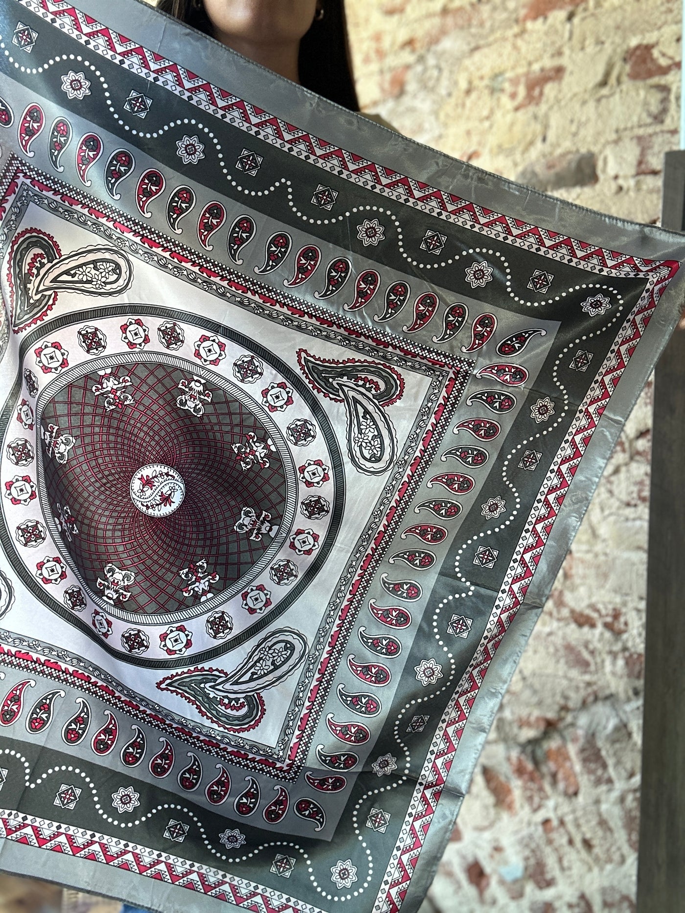 Details of the geometric and paisley pattern of our Rossio Paisley Wild Rag [Grey & Pink] while being held in the air.