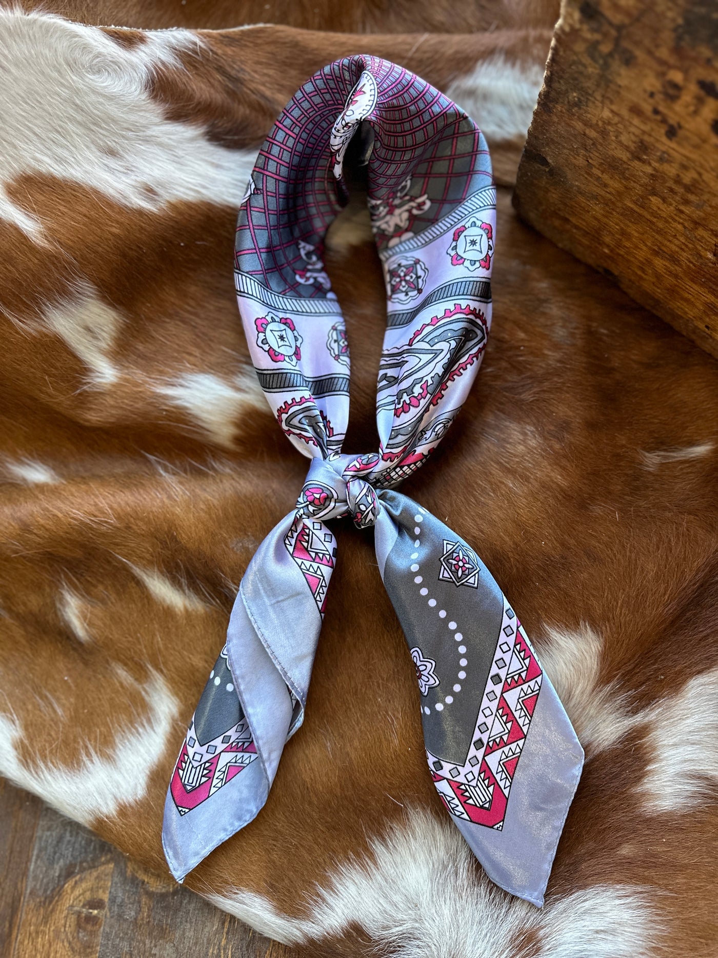 Rossio Paisley Wild Rag [Grey & Pink] on a cowhide backdrop, tied as a scarf.