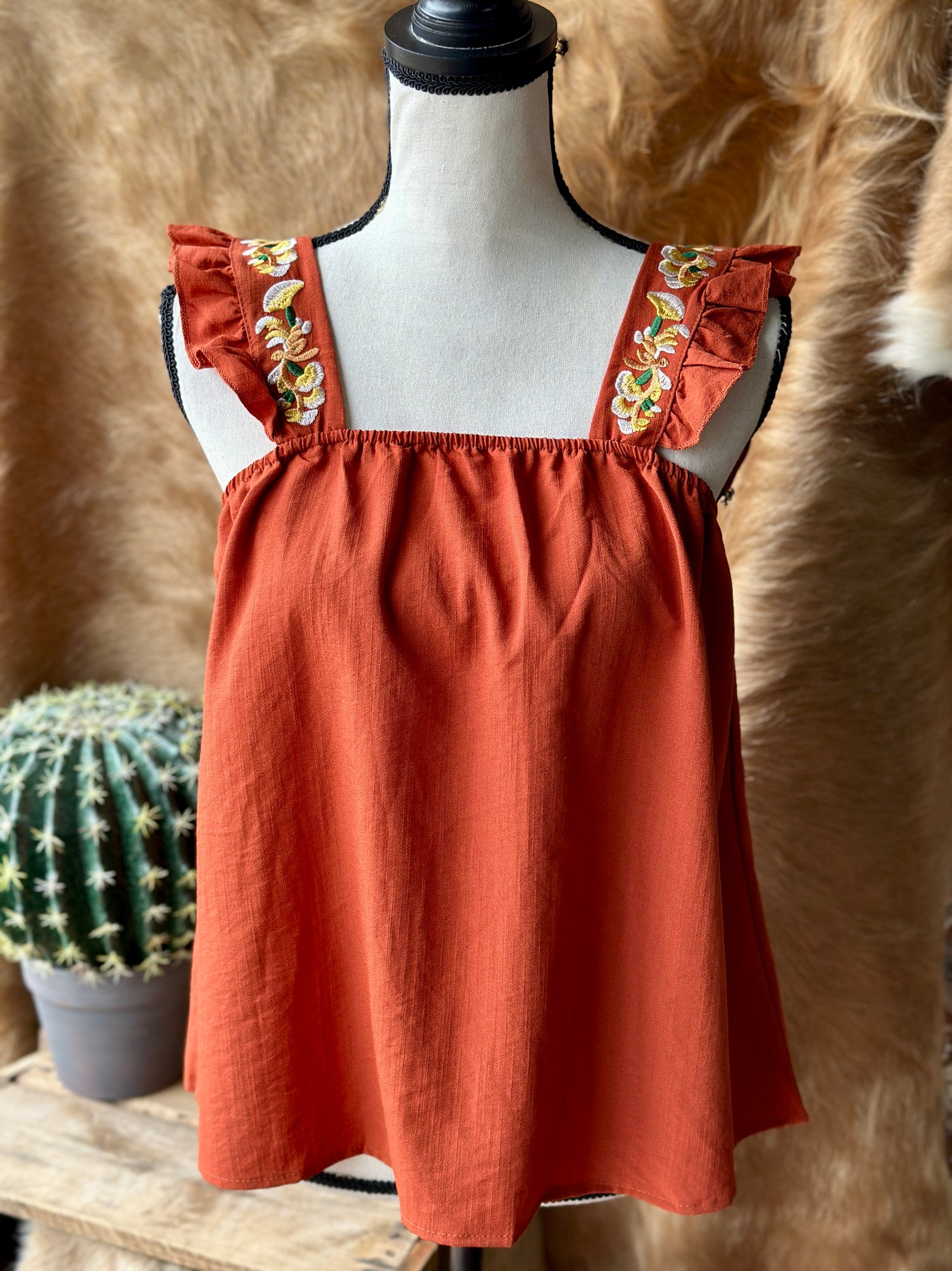 Feminine and Western-inspired, the Gertrud Embroidered Ruffle Sleeve Tank in Rust is a must-have for any modern cowgirl.