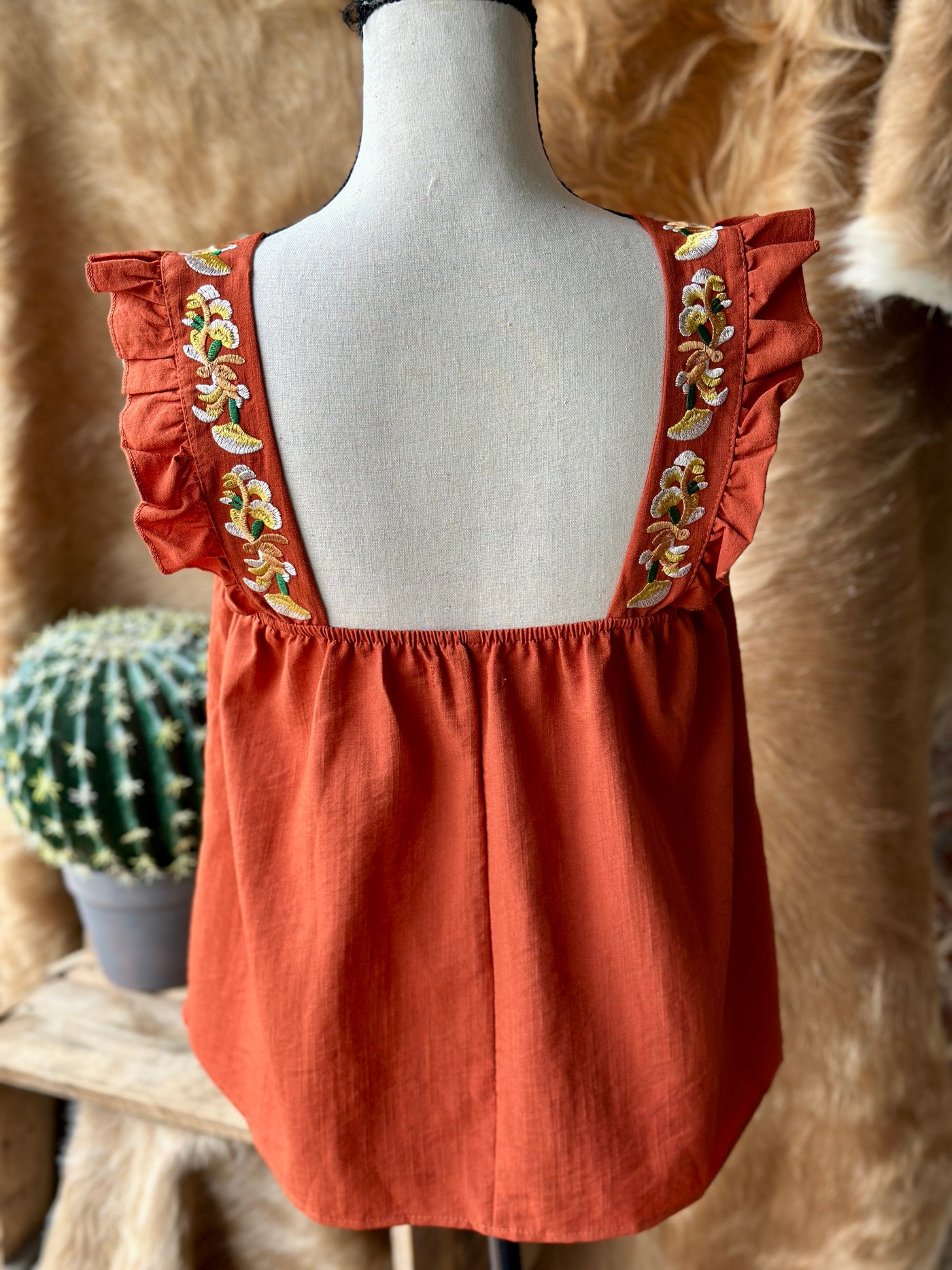 Rust-colored Gertrud Embroidered Ruffle Sleeve Tank with floral embroidery adds a touch of vintage romance to your wardrobe.