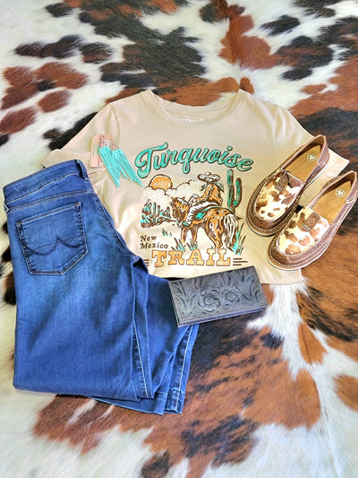 Flatlay photo of the Gideon Turquoise Trail Graphic Tee, denim jeans, and Cow print Ariat Cruiser Slip On Shoe [Tan Floral Emboss Brindle Hair on Hide] for an easy everyday Western outfit.