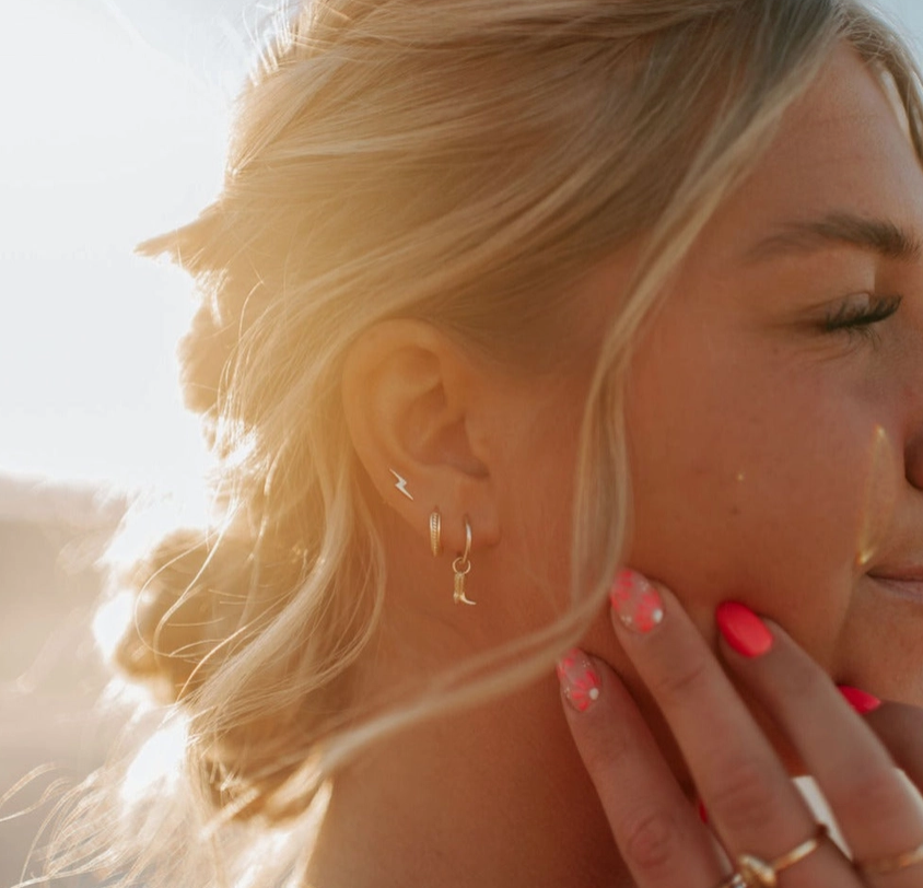 A model channeling her inner champion with the Hailey Cowboy Boot Hoop Earrings paired with a gold huggie and a gold lightning bolt earring.