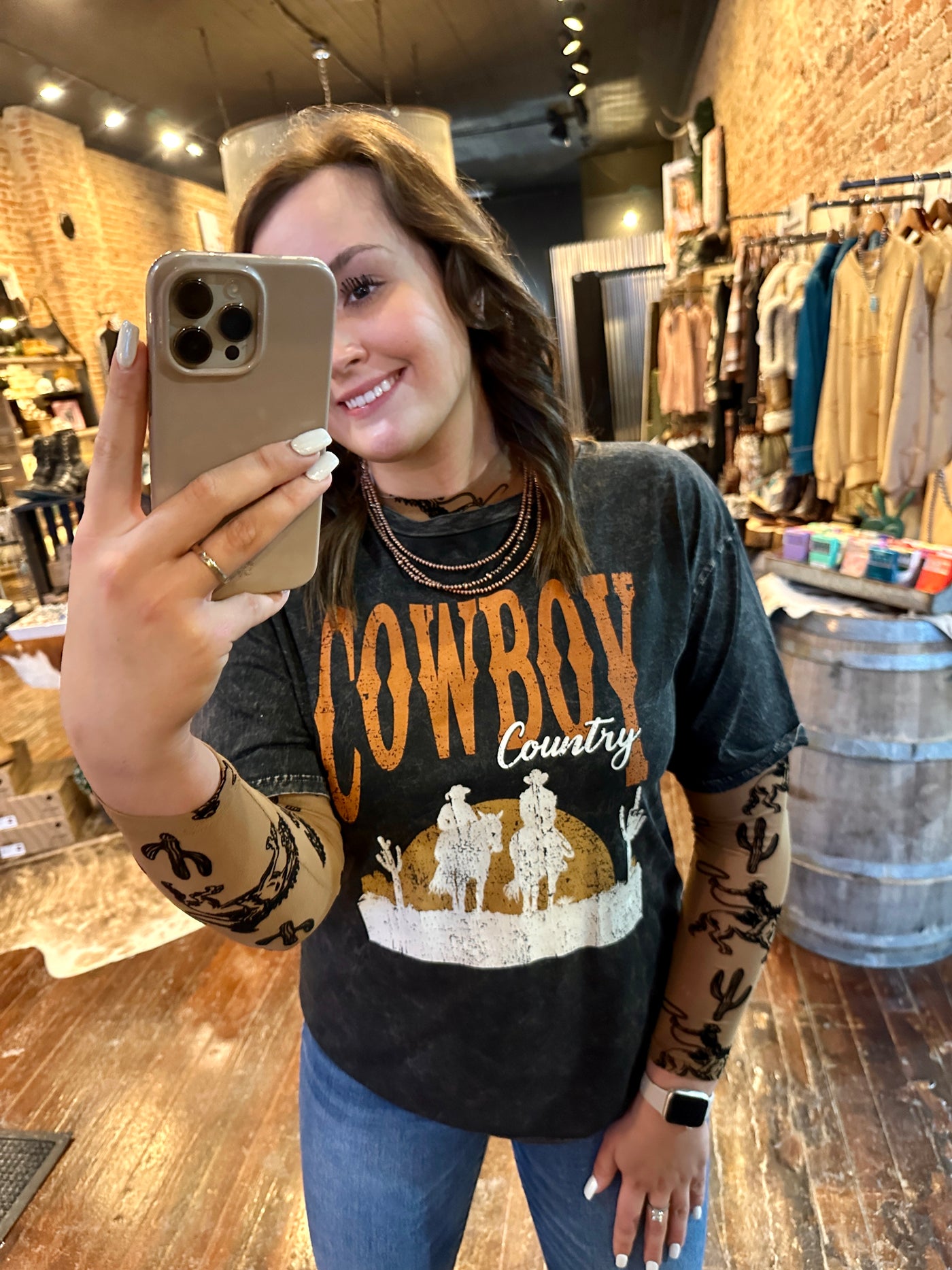 Holly Cactus & Cowboys Long Sleeve Mesh Top featuring a warm brown base with bold black raised patterns of cacti and cowboys riding with lassos.