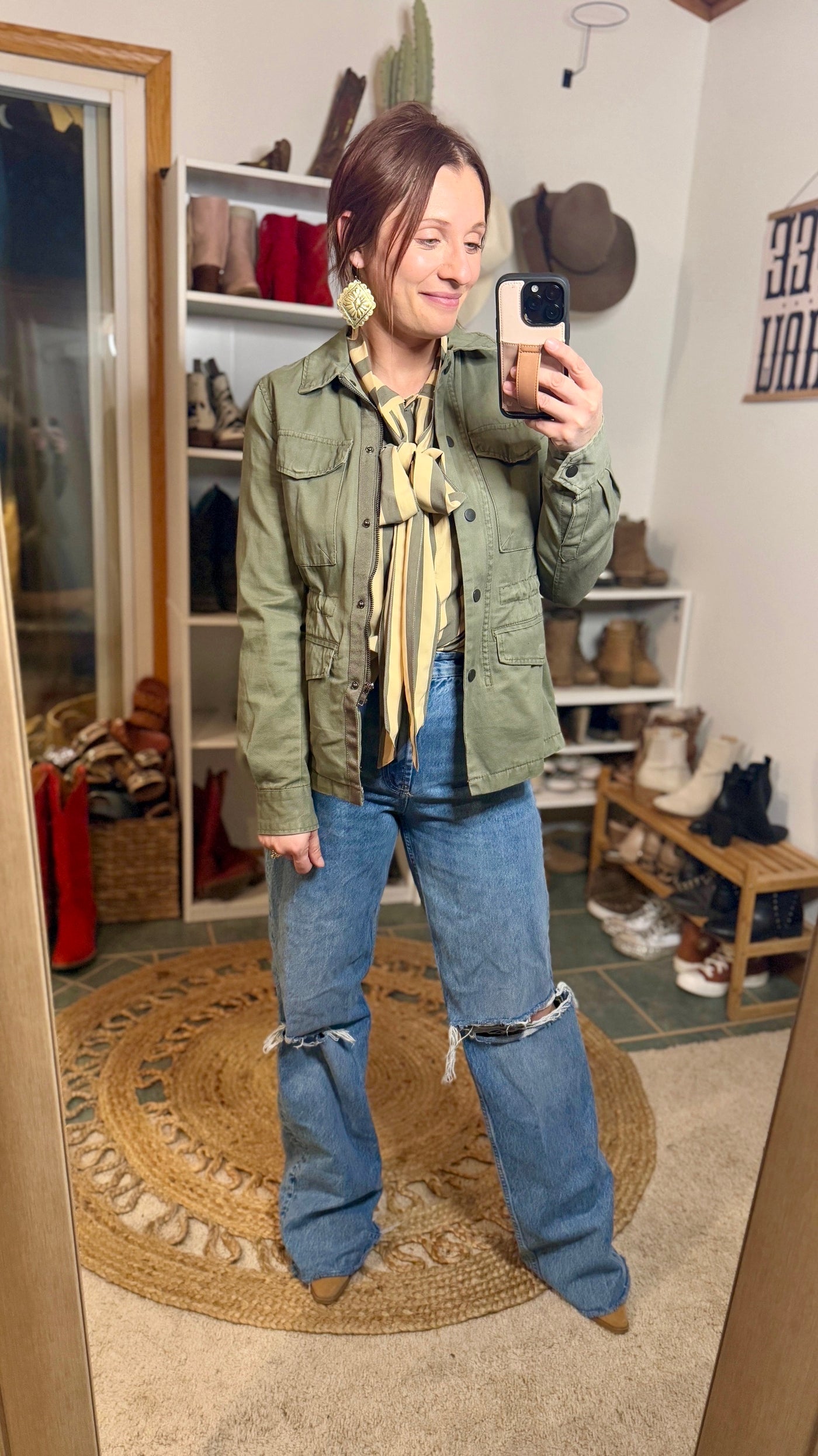 Model wearing Kallyn Striped Bowtie Blouse paired with denim and a coordinating olive green bomber jacket and statement earrings for a funky afternoon look.