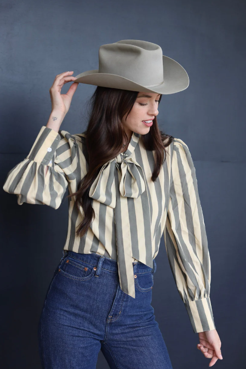 Model adjusting her cowboy hat paired with the Kallyn Striped Blouse for a playful yet elegant touch.