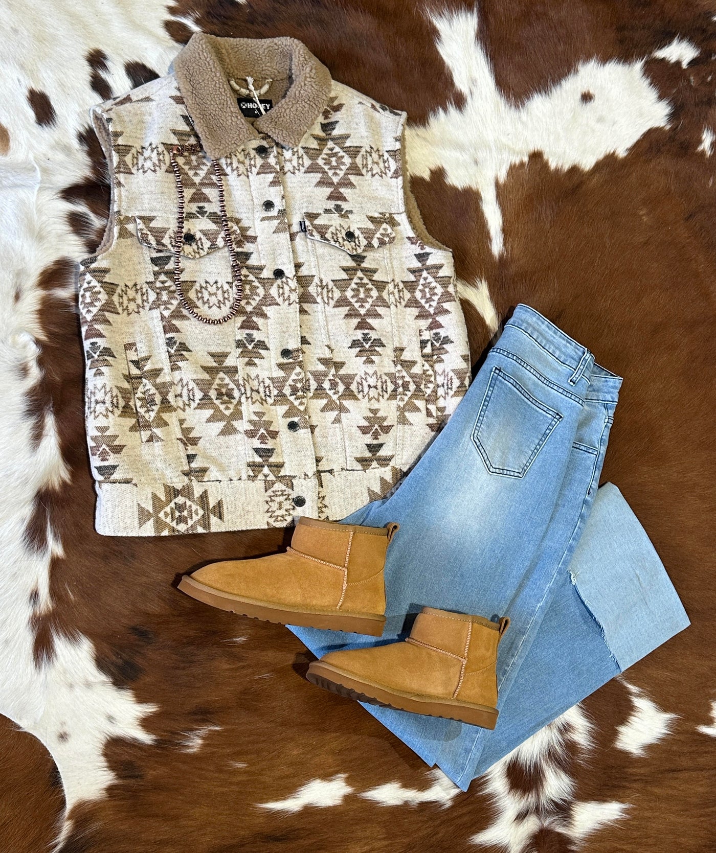 Flatlay view featuring our Lamo Kora Moccasin Mini Boots with jeans and an Aztec Vest.