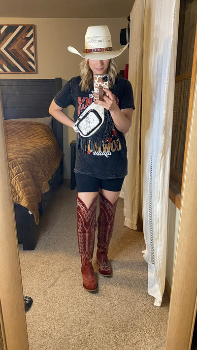 Broker Leather employee modeling the Lane Lexington Over-the-Knee Boots [Smoldering Ruby] with a graphic tee, cowboy hat, and biker shorts.