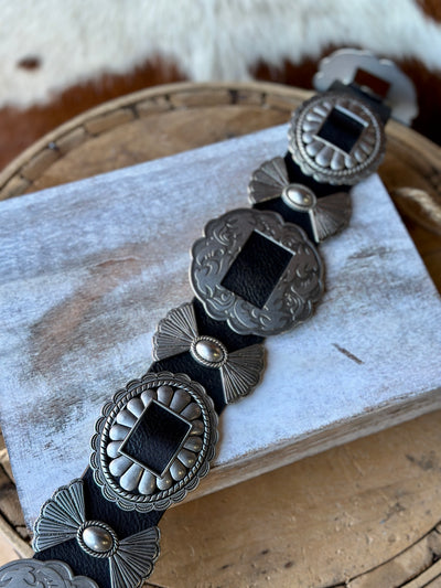 Close-up of removable silver conchos on a black leather belt.