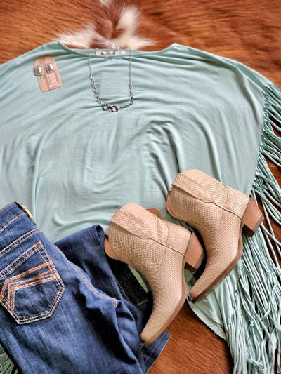 Flat lay outfit western-inspired fringe top styled with boots and jeans for a rodeo-ready outfit in washed seafoam.