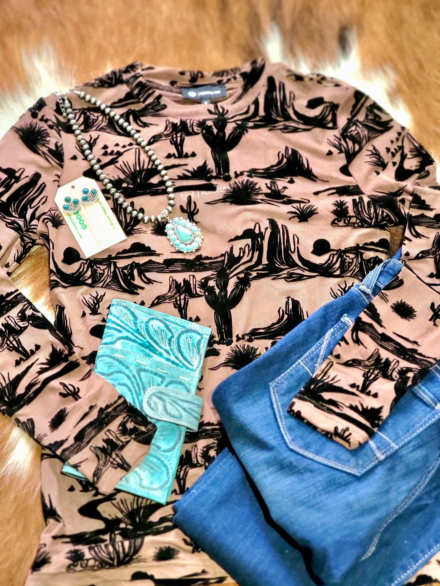 Macee Desert Scene Mesh Top featuring a detailed desert landscape with cacti and mountains paired with jeans, a turquoise necklace, and a tooled leather wallet.