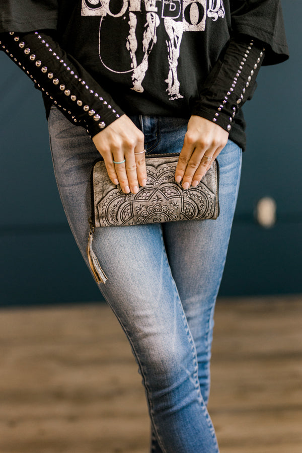 Hand-tooled genuine leather wristlet with mandala design and zipper closure held by model for size relevance.