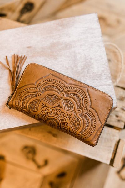 Natural tooled leather wristlet with floral mandala design and wrist strap.