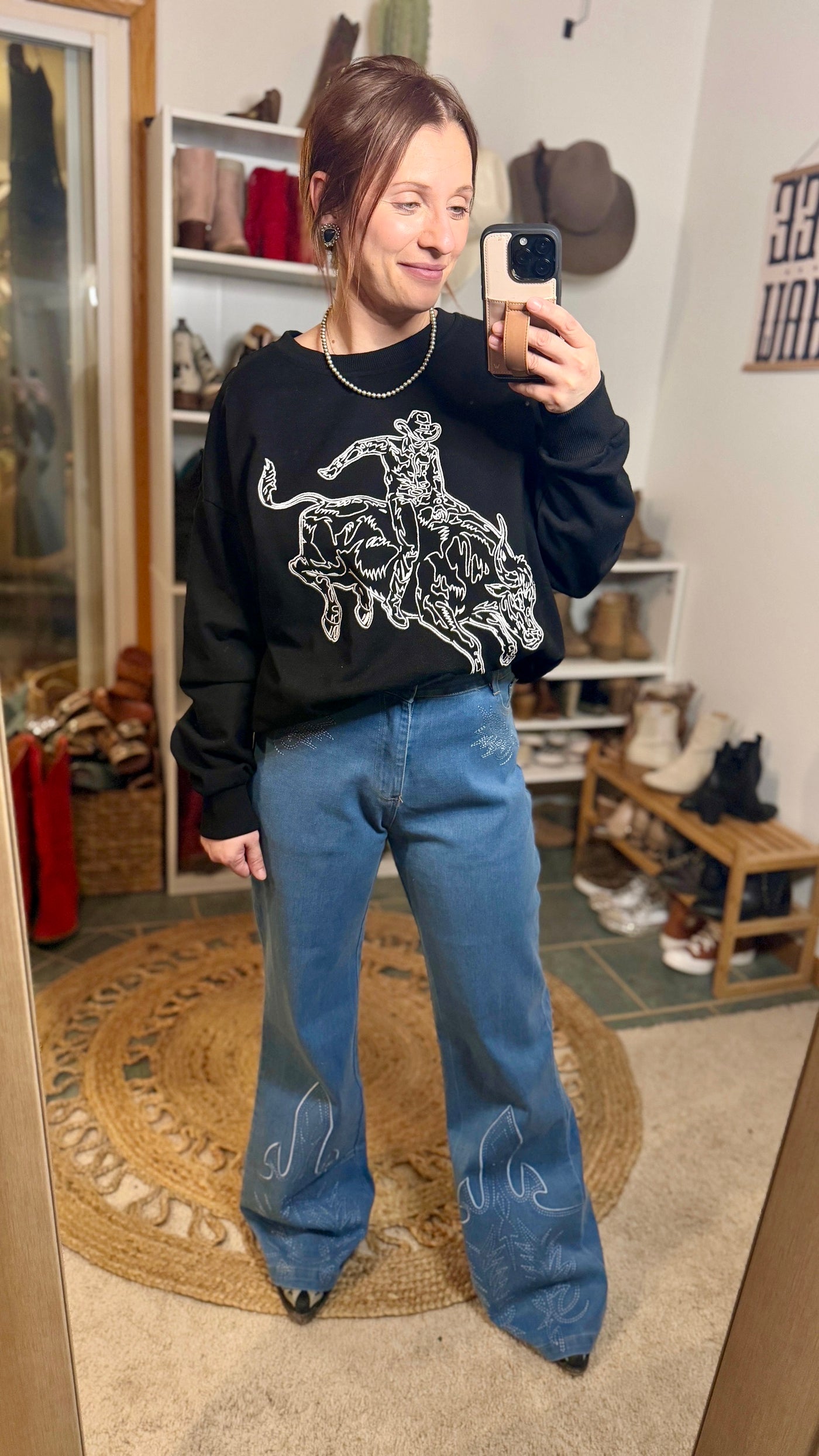 Cowgirl wearing Mauney Bull Rider crewneck paired with jeans and boots.