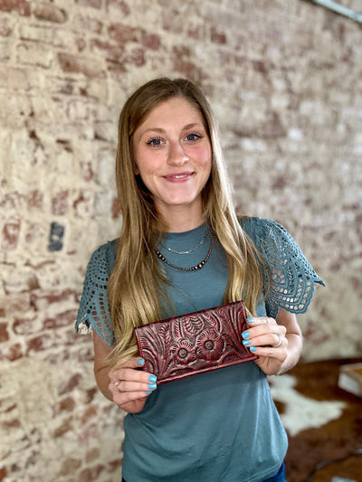 Hand-tooled oxblood red leather McCrae Tooled Slim Checkbook Cover held by Broker Leather employee for size reference.