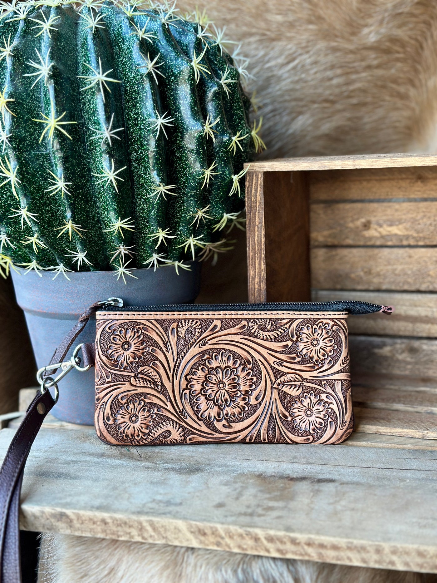 Western-inspired tooled leather wristlet with removable strap and secure zippered pouch.