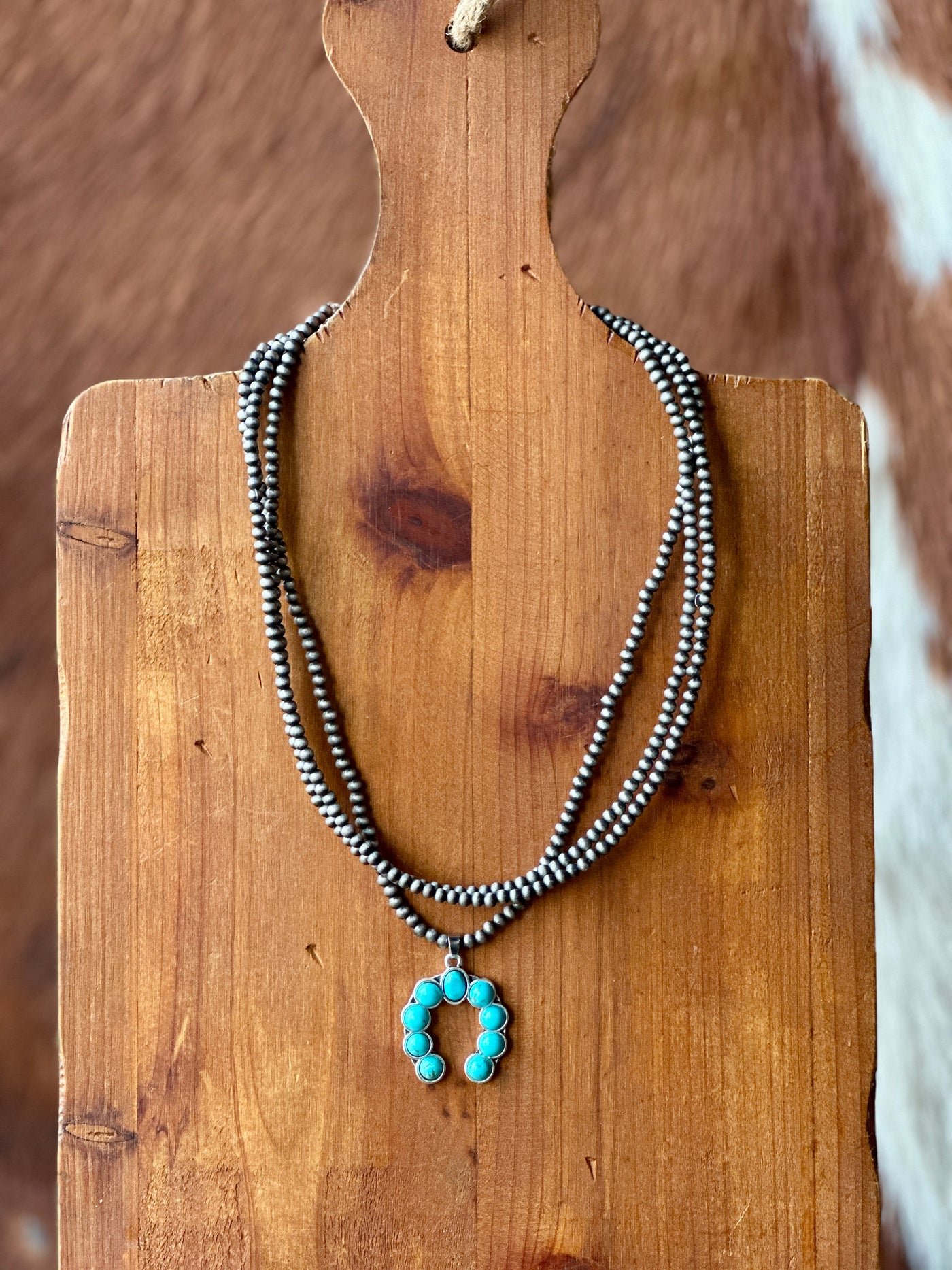 Broker Leather's Mia Squash Turquoise Necklace hanging on a wooden board showcasing its unique pendant and versatility in the Western World.