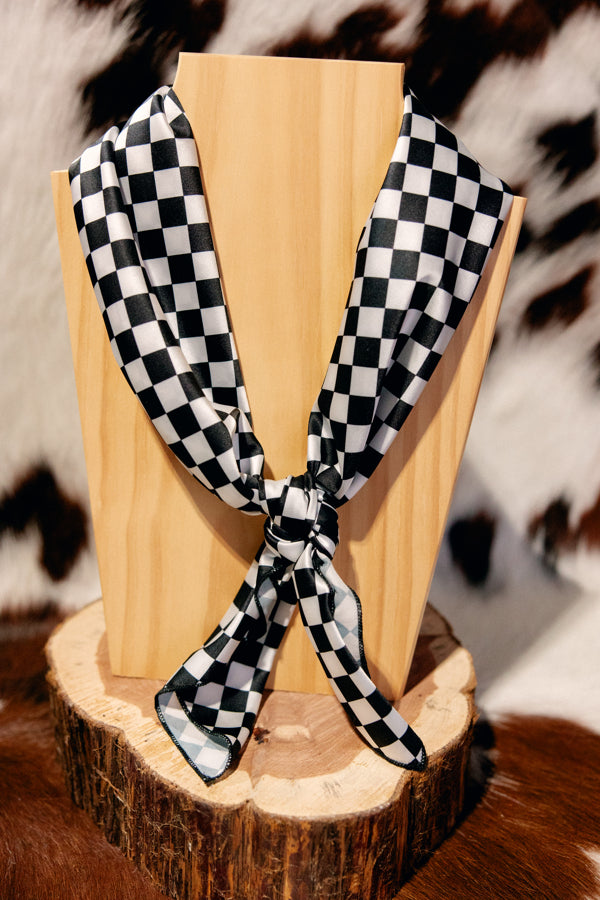 Black and white checkered wild rag tied neatly in a 4-square knot on a wooden neckboard.