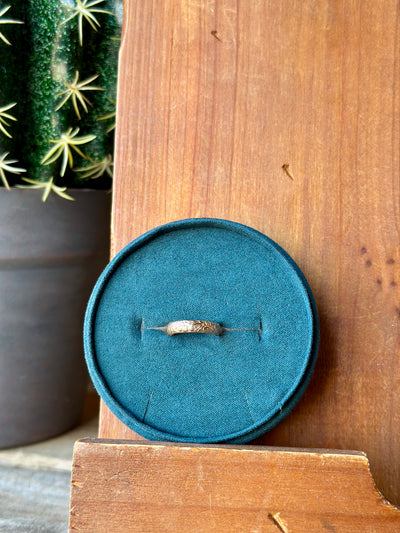 Gold stacker ring with Western floral engravings displayed on a rustic background.