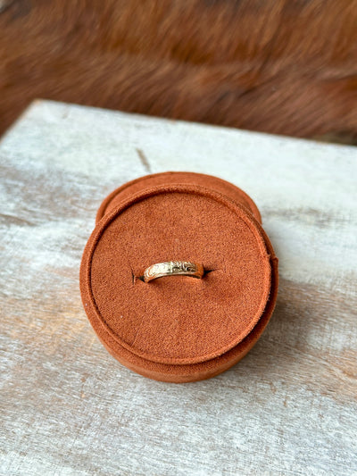 Gold stacker ring with Western floral engravings displayed on a rustic background.