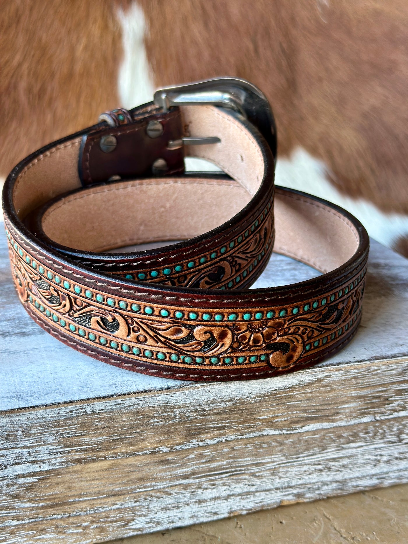 A brown Genuine Lather Belt with Hand-Tooled Floral Pattern with hand-painted turquoise accents.