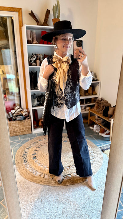 Front view of the Open Gate S&P Cowhide Vest on a model paired with a white button down dress, western scarf, black jeans and a black hat.