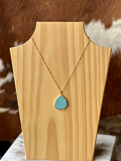 Turquoise and gold pendant necklace resting on weathered wood for a Western aesthetic.