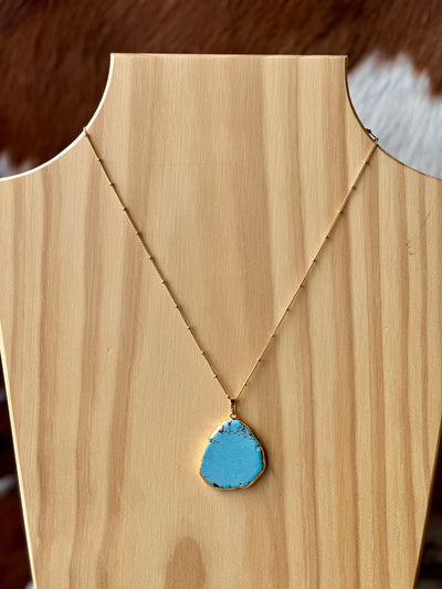 Western-inspired turquoise pendant necklace displayed on a rustic wooden background.