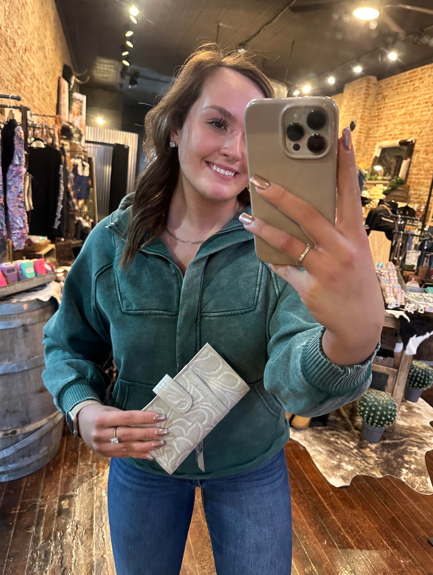 A Broker Leather employee modeling the Ricardo Floral Tooled Organized Wallet [Bone] to show that it measures approx. 7.75" x 4.25".