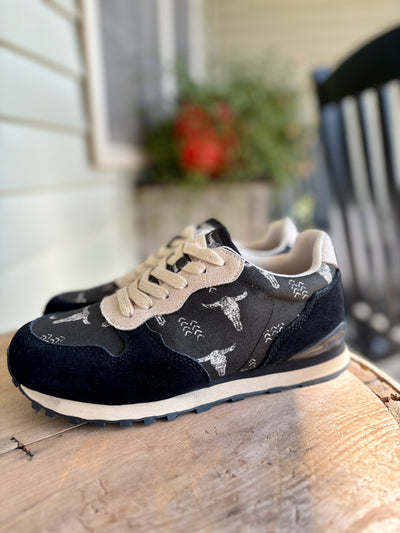 Black sneakers with white bull skull/longhorn patterns on a wooden surface