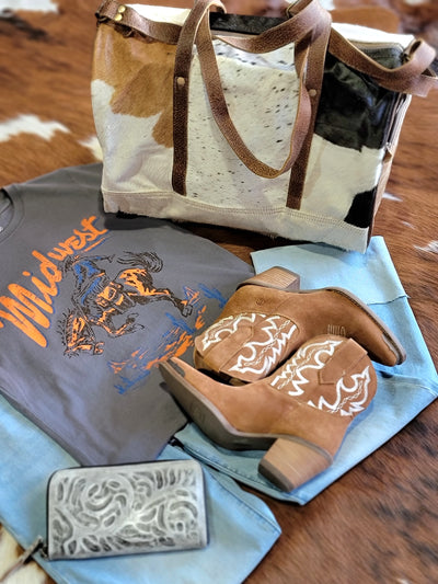 Flatlay picture of our Sigmund Cowhide & Leather Weekender Bag with a graphic tee and boots.